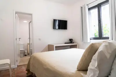 a white bedroom with a bed and a tv on the wall at Casa das Proteas in São Jorge
