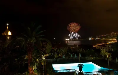 a night view of a pool with fireworks in the background at Hotel Quinta Bela S Tiago in Funchal