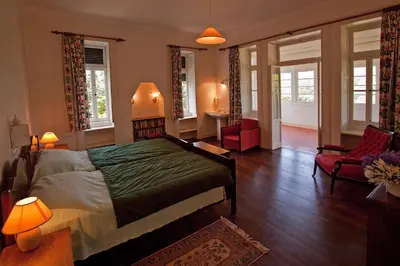 a bedroom with a bed and two chairs and windows at Quinta das Colmeias in Santo da Serra