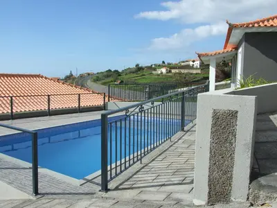 a swimming pool with a black fence and a blue water at Paraiso das Flores in Estreito da Calheta