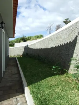 a brick wall with a green yard next to a building at Paraiso das Flores in Estreito da Calheta