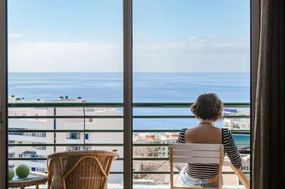 a woman sitting in a chair looking out a window at the ocean at Ajuda III by An Island Apart in Funchal