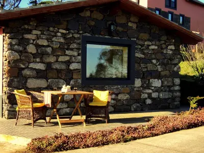 a table and chairs in front of a stone wall at Palheiro do Avô in Santa Cruz