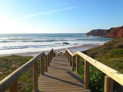 a wooden boardwalk leading to a beach with the ocean at Villa Nooma in Carrapateira