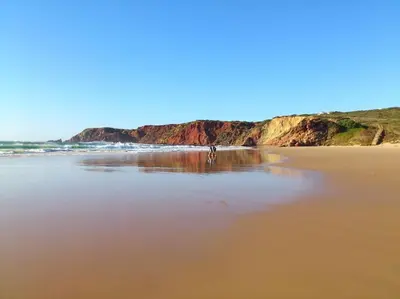 a beach with a person walking on the sand at Villa Nooma in Carrapateira