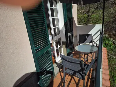 a balcony with a table and a chair and an umbrella at Valley of Nuns Holiday Apartments in Curral das Freiras