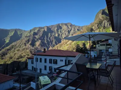a balcony with a table and an umbrella and mountains at Valley of Nuns Holiday Apartments in Curral das Freiras
