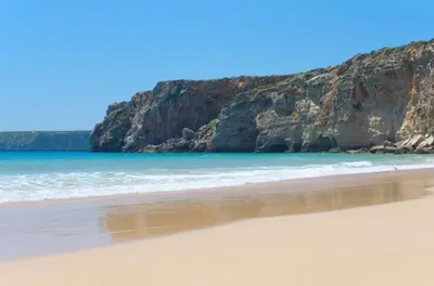 a beach with the ocean and cliffs in the background at Sea Sagres in Sagres