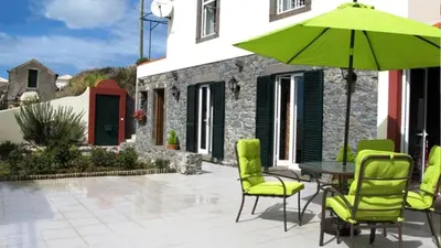 a patio with a table and chairs and a green umbrella at Casa dos Serrões in Calheta