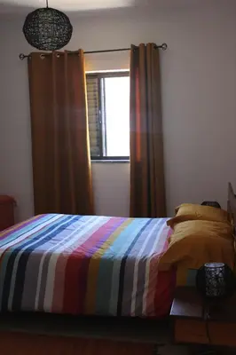 a bedroom with a bed with a colorful blanket and a window at Abrigo das Nortadas in Vila do Bispo