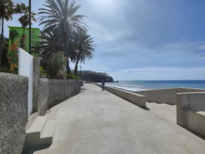a person walking down a sidewalk next to the beach at By the Beach & Pool Apartment in Funchal