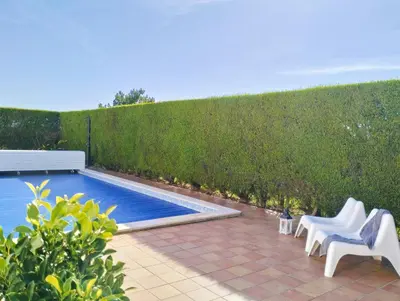 a swimming pool with two white chairs next to a hedge at VILLA ANDORINHA with Private Pool in a quiet area in Aljezur