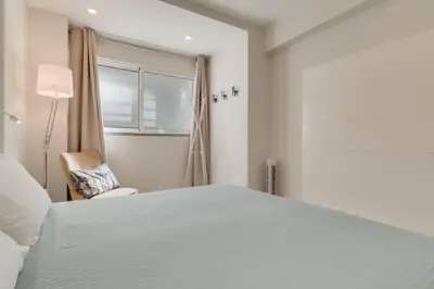 a white bedroom with a bed and a chair at Braganza apartment in Funchal