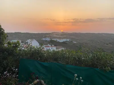 a person standing on a hill with the sunset in the background at Apartamento Miradouro in Carrapateira