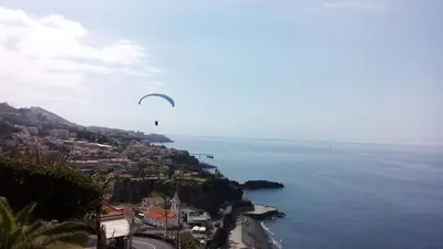 a person flying a kite over the ocean with a city at The Best Atlantic Ocean View in Câmara de Lobos