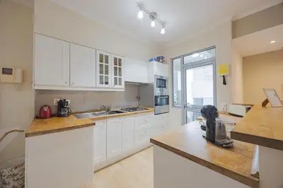 a kitchen with white cabinets and a large window at Central Funchal Apartment - GARDEN - Free Parking & AC in Funchal