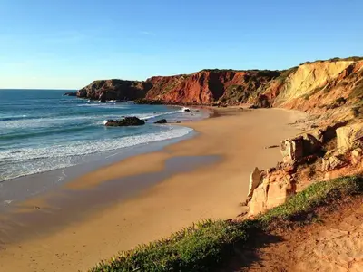a sandy beach with the ocean and cliffs at Varandas - Arrifana, com piscina, junto à praia in Praia da Arrifana