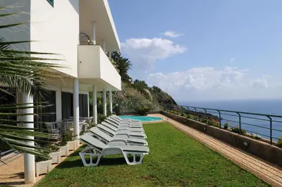 a group of lounge chairs next to a house with the ocean at An uninterrupted 180 overlooking the Atlantic Ocean in Caniço