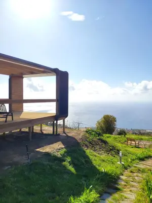 a wooden bench sitting on top of a field with the ocean at Calheta Glamping Pods - Nature Retreat in Calheta