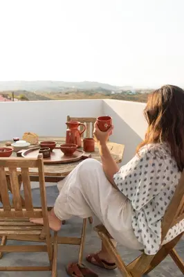 a woman sitting in a chair drinking from a mug at Casa Bombordo in Carrapateira