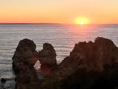 a sunset over the ocean with rocks in the water at Magnolia Mar Apartamentos in Lagos