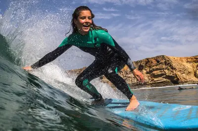 a woman riding a wave on a surfboard in the ocean at Sagres Natura in Sagres