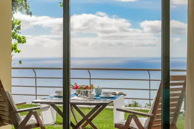 a table on the balcony with a view of the ocean at Casa do Papagaio Verde in Funchal