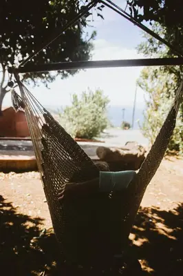 a person laying in a hammock in a yard at Madeira Sunset Cottage - Nature Retreat in Ponta do Pargo