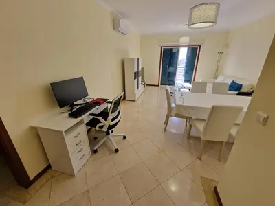 a living room with a table and a woman sitting on a balcony at Forum Madeira Ajuda Apartment in Funchal