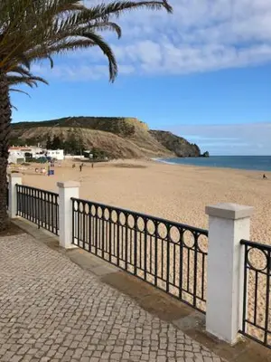 a beach with a black fence and a palm tree at Luz casas- BayLuz apart,pool,beach, tennis, wifi,aircon in Luz