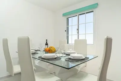 a white dining room with a glass table and white chairs at Casa Campos , Modern two bedroom house in Loreto in Achada de Cima