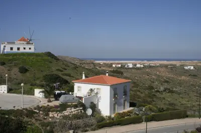 a house on a hill with a windmill in the background at Sea View Apartment Carrapateira in Carrapateira
