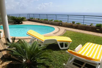 two chairs and a swimming pool with the ocean in the background at Vivenda Belo Horizonte in Caniço