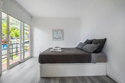 a white bedroom with a bed and a large window at Magical Sunset in Madalena do Mar