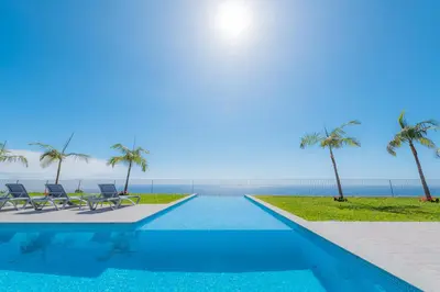 a swimming pool with two chairs and palm trees at Engenho Velho Hotel & Restaurante - Adults Only in Arco da Calheta