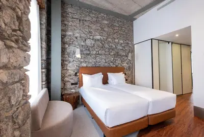 a bedroom with a white bed and a stone wall at Hotel Cajú in Funchal