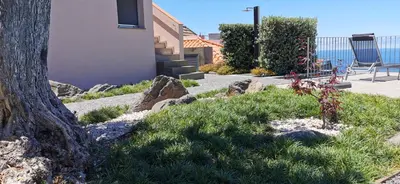 a building with a tree and some grass and rocks at Casa Atlantico Dachterrassengeschoss in Ribeira Brava