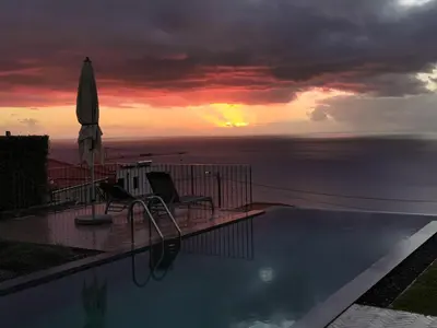 a swimming pool with an umbrella and chairs and the ocean at Casa Atlantico tropischer Seitenflügel in Ribeira Brava
