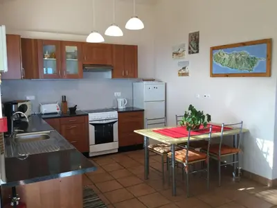 a kitchen with a table with chairs and a stove at Banda Do Sol Self Catering Cottages in Estreito da Calheta
