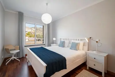 a white bedroom with a bed and a chair and a window at Reis Magos III by An Island Apart in Caniço