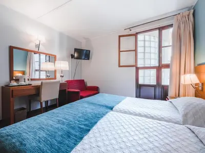 a hotel room with a bed and a desk and a chair at Hotel Vila Bela in Porto da Cruz