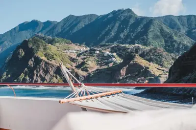a hammock on a boat with mountains in the background at Hotel Vila Bela in Porto da Cruz