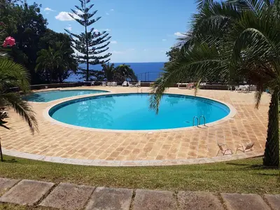 a swimming pool with two chairs and the ocean at Listen the sound of the Sea - The Sunset of your Dreams in Funchal