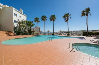 a swimming pool with palm trees and a building at Two Bedroom Apartment Vila Mos Lagos in Porto de Mós
