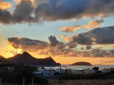 a sunset over the ocean with houses and mountains at Quintinha das Lombas S in Porto Santo