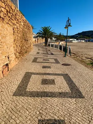 a brick sidewalk next to a wall with palm trees at St. James Beach & Pool Apartment in Luz