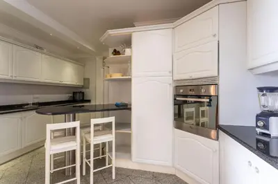 a white kitchen with white cabinets and stools at FLH Vivenda Belo Horizonte with Sea View in Caniço