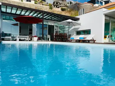 a swimming pool with a red umbrella and a house at Villa Mar Garajau in Caniço