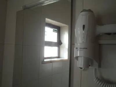 a bathroom with a window and a hair dryer on the wall at Quartos Maria Clara in Sagres