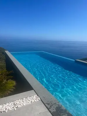 a blue swimming pool with the ocean in the background at Apartamento MAR AZUL in Calheta